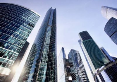 Office and residential skyscrapers against bright sun and clear blue sky. Commercial real estate. Glass and metal in urban architecture. High-tech facade design. Modern business city district. Office buildings exterior. Financial city district. Reflections and highlights in glass. Wide angle city photography.